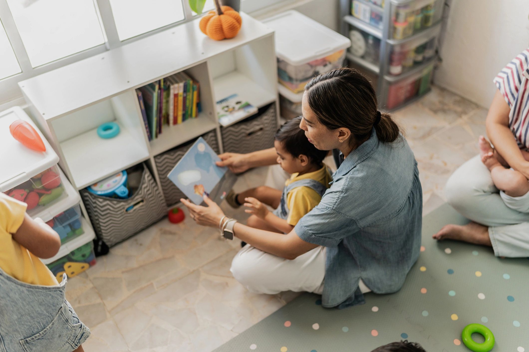 Parent reading a picture book with a toddler in a playroom